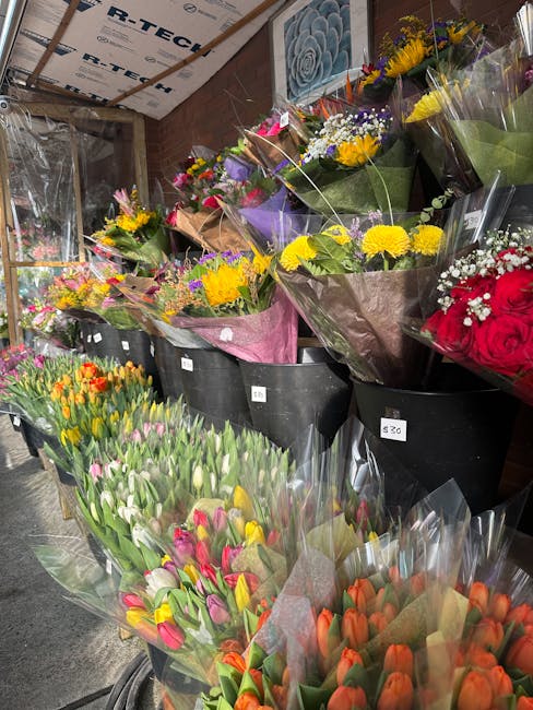 A display of fresh floral bouquets arranged in black buckets inside a flower shop. The bouquets feature a variety of vibrant flowers including yellow chrysanthemums, purple irises, pink tulips, orange