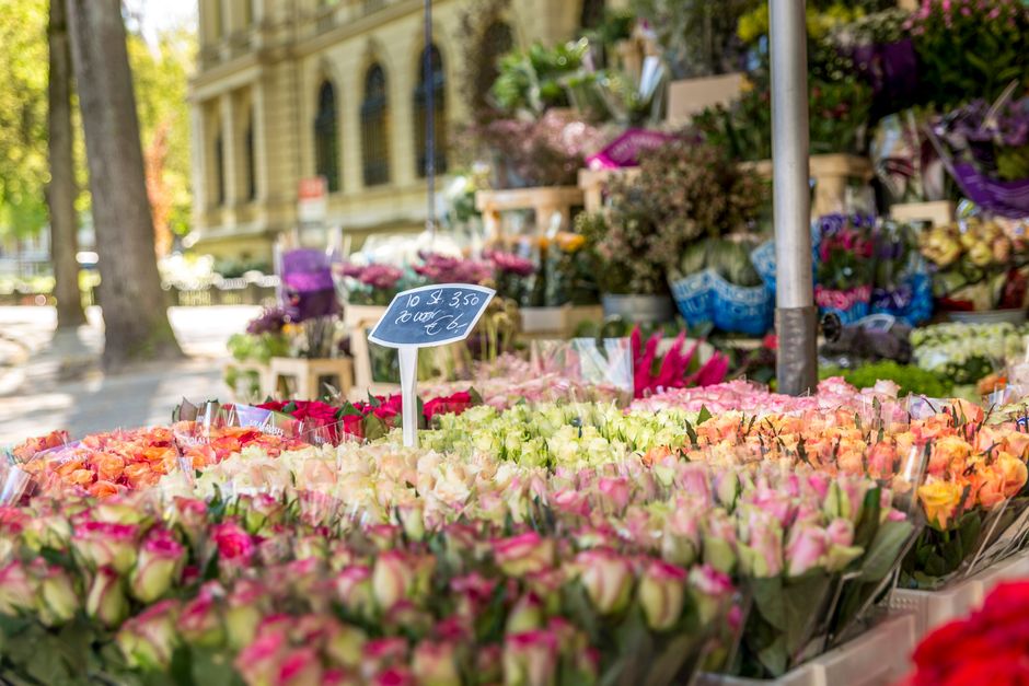At an outdoor flower stall operated by floristkennington.co.uk, a vibrant display of fresh flowers includes pink, peach, and white roses arranged in bouquets with lush green foliage. The flowers are w